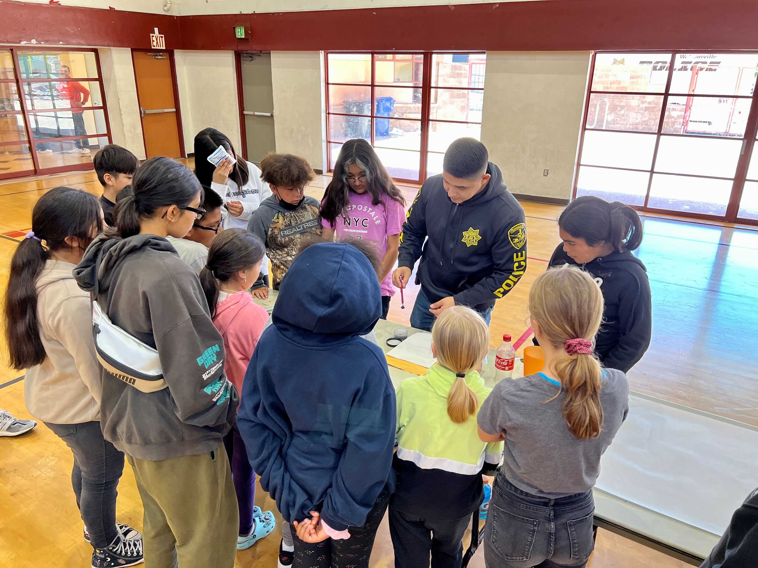 Teens around a table where a speaker is demonstrating something
