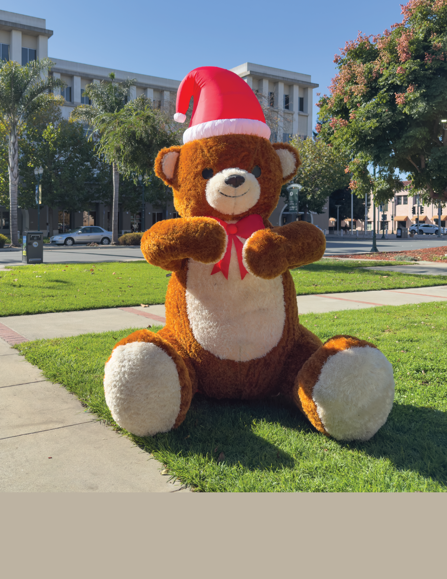 Giant blow up teddy bear with Christmas hat in front of City building 