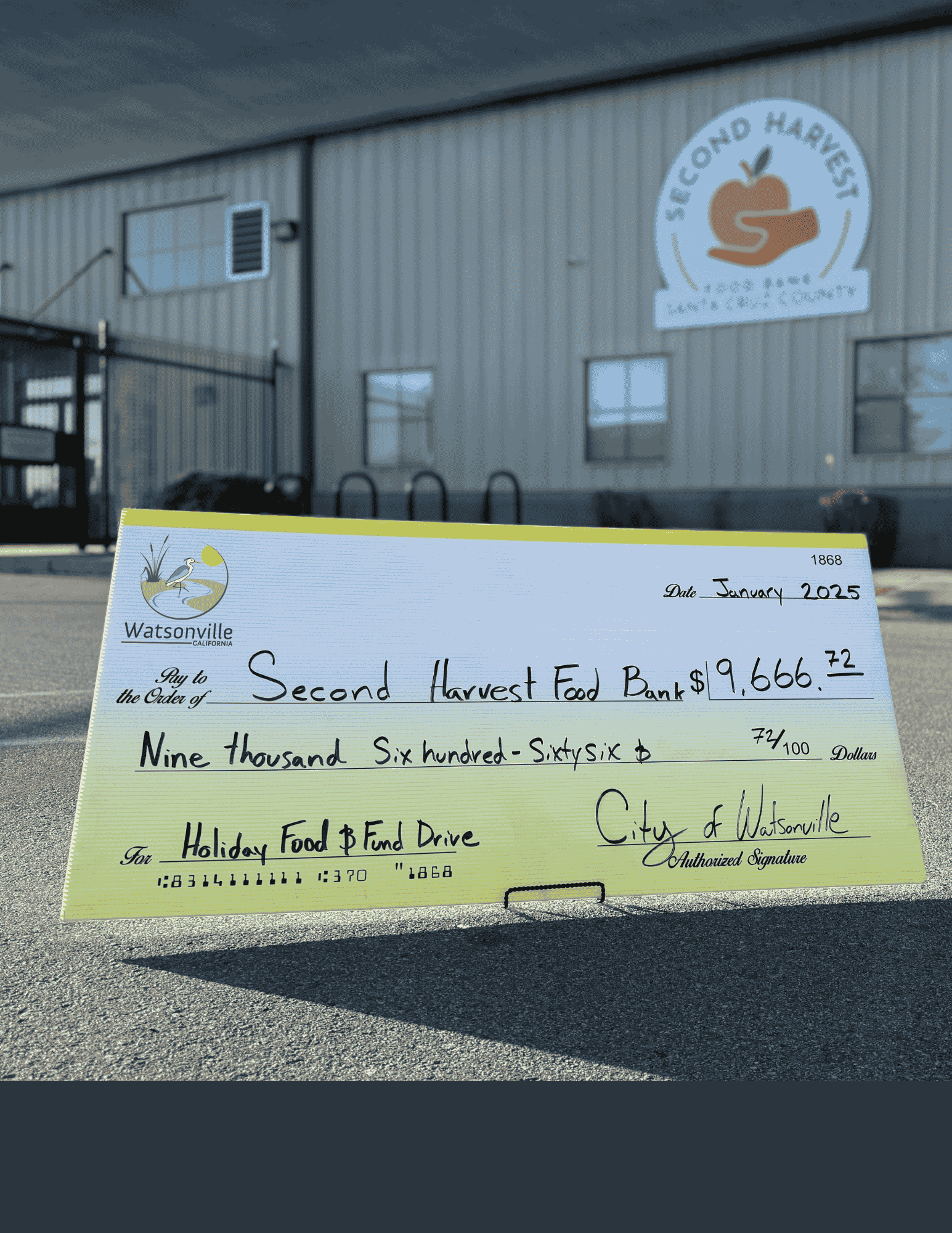 Large check for more than $9,000 propped in front of food bank sign 