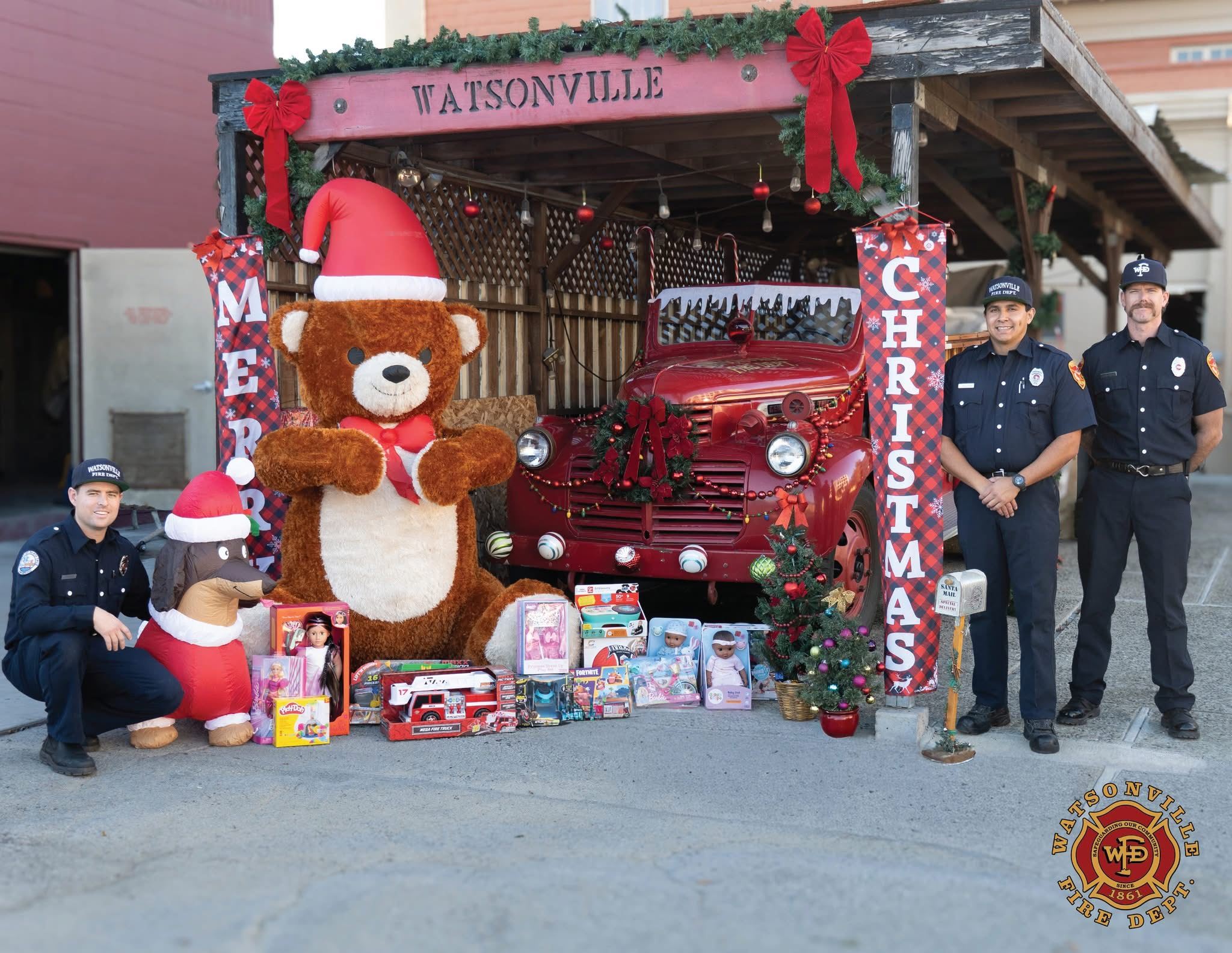 Firefighters posing for a festive photo with Christmas inflatables and an antique firetruck